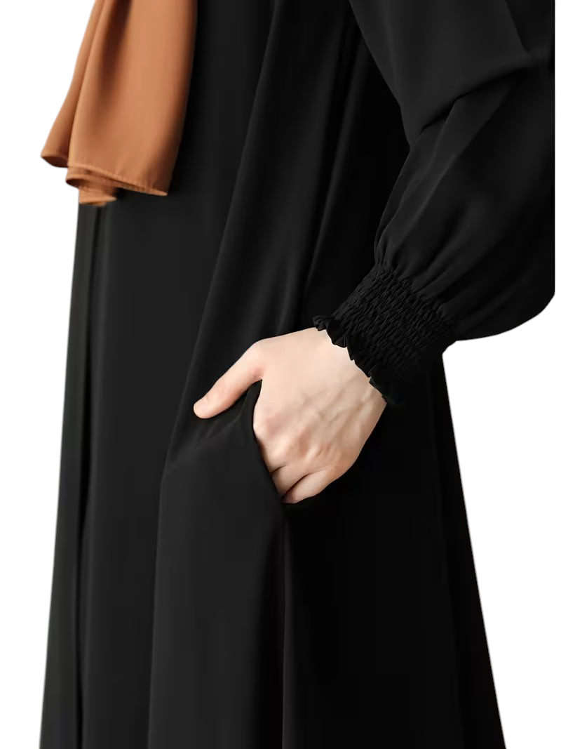 Linen & Loom black abaya with long sleeves, smocked cuffs, and side pockets, styled with a brown hijab.