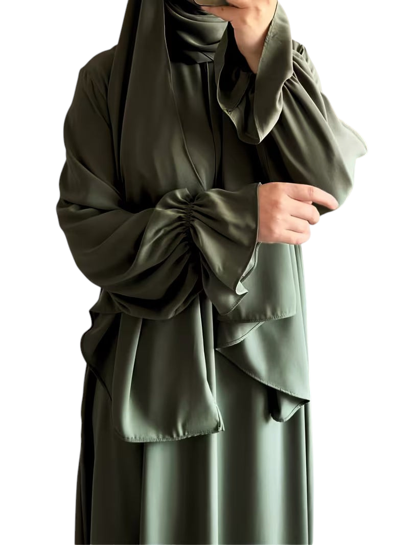 Linen & Loom olive green one-piece abaya with elegant bell sleeves and a matching hijab in a bright indoor setting