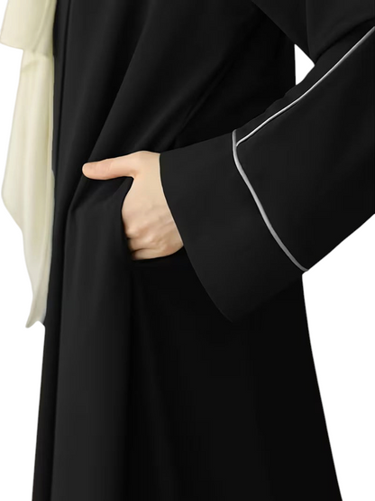 Linen & Loom black abaya featuring a loose fit, long sleeves with subtle grey piping, and a convenient side pocket.