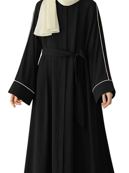Linen & Loom black abaya with white piping detail, long sleeves, and a matching waist tie worn with a cream hijab.