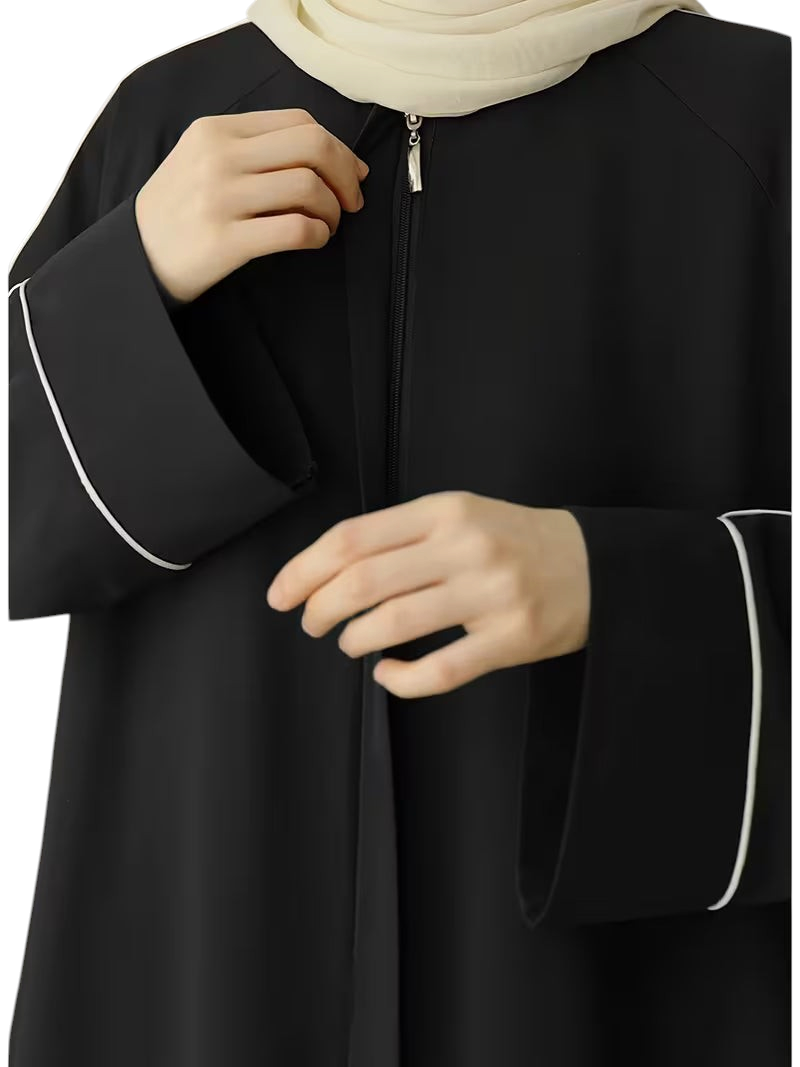 Linen & Loom black abaya with white piping detail and front zipper, worn with a cream hijab for a modest look.