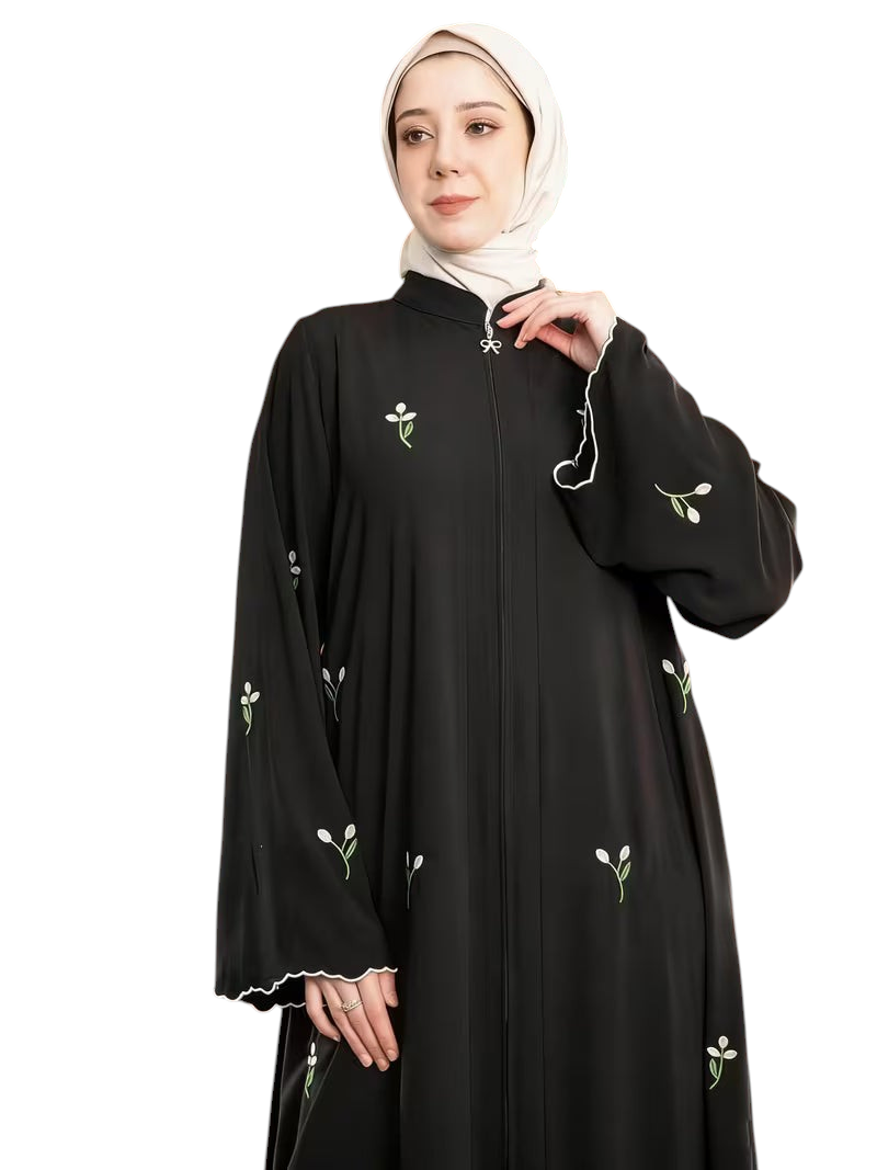 Linen & Loom black abaya with white floral embroidery, front zipper, and scalloped sleeves worn by a woman in a hijab.