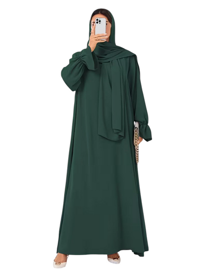 Linen & Loom dark green one-piece abaya with elegant bell sleeves and matching hijab, worn by a woman in a bright room.