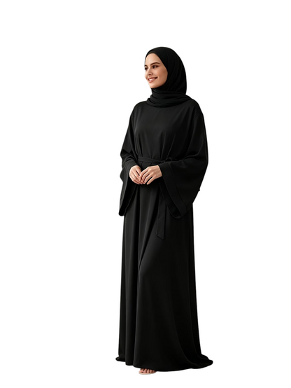 Linen & Loom black wide-sleeve belted abaya worn by a smiling woman in a bright, minimalist living room setting.