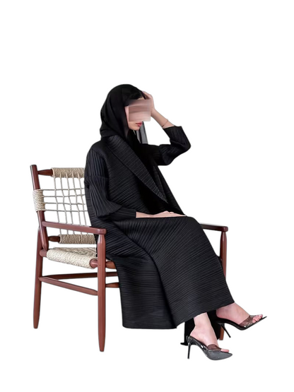 Linen & Loom black plisse abaya with long sleeves and loose fit, worn by a woman sitting on a wooden chair.
