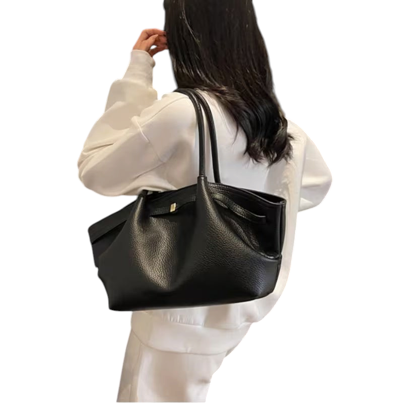 Linen & Loom black leather tote handbag with double handles worn over the shoulder by a woman in a white outfit.